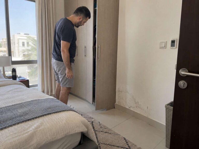 Person investigating a damp wall area in a home with subtle signs of hidden moisture.