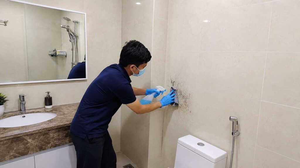 A man cleaning black mold spots in a bathroom