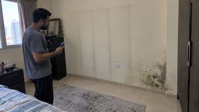 Homeowner examining irregular mold-like stains and dry ghosting marks on a wall in a UAE apartment