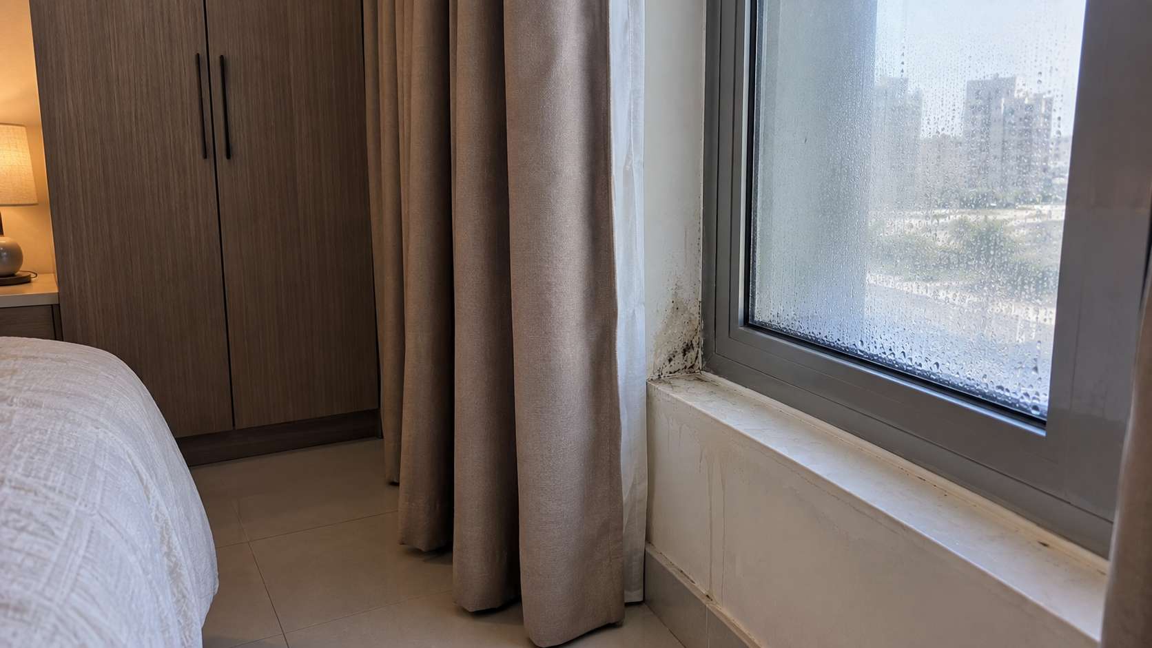 Closed curtains trapping condensation around a sealed window frame in a UAE bedroom