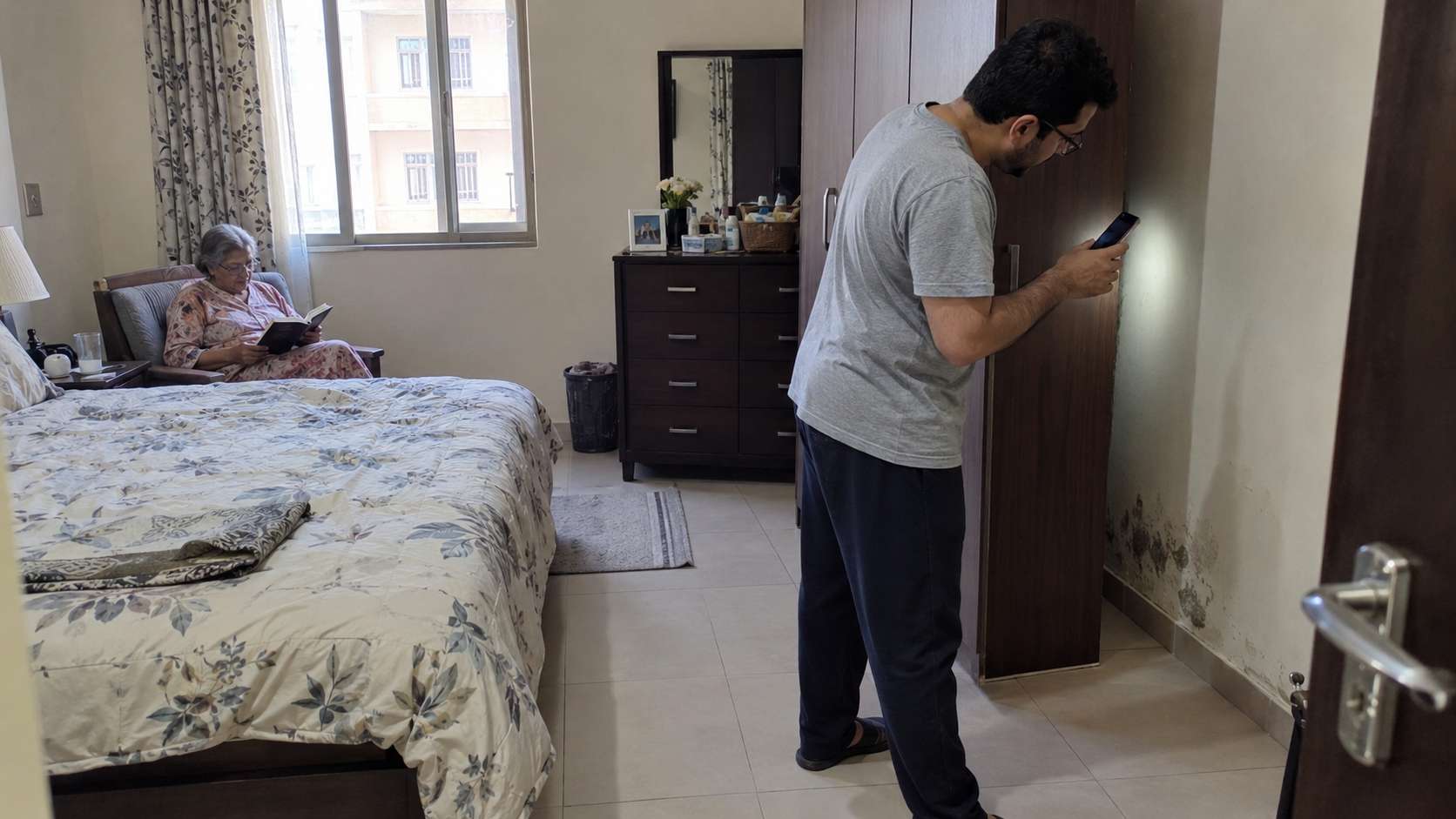 Family member checking behind a wardrobe for dampness and early mold while an elderly resident stays away
