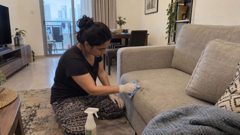 Homeowner cleaning a small mold patch on a fabric couch with an upholstery-safe cleaner