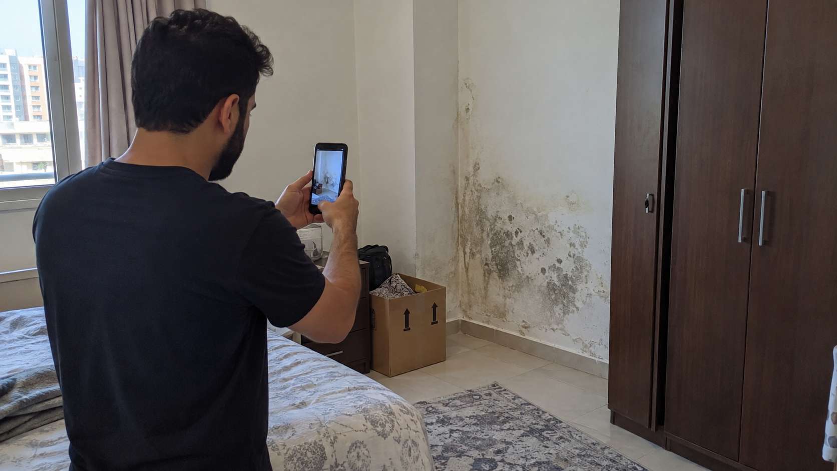 Homeowner photographing localized mold and moisture damage on a wall in a recently purchased apartment.