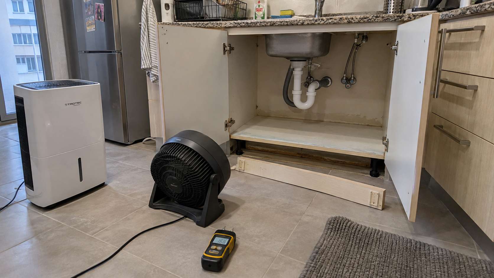 Open under-sink cabinet and removed kickboard drying hidden moisture after a leak in a UAE kitchen