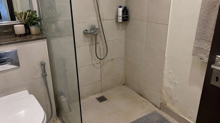 Subtle cracked grout, failed caulk, and damp warning signs around a shower wall in a UAE bathroom
