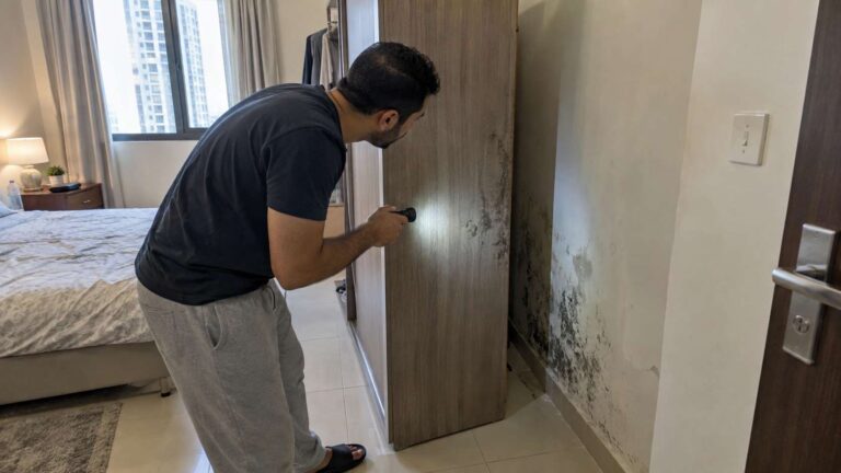 Homeowner discovering hidden mold behind a wardrobe in a UAE bedroom