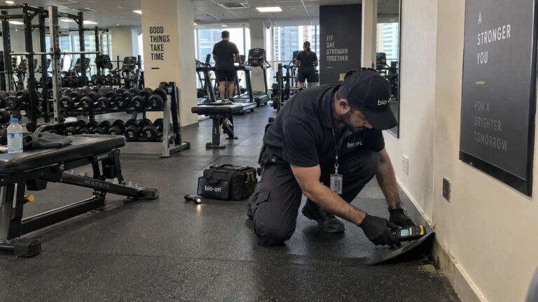 Bio-On technician checking for moisture inside a commercial gym with rubber flooring and fitness equipment.