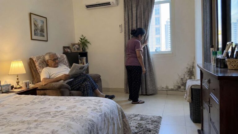 Elderly resident in a UAE home with localized mold and moisture damage visible on a nearby wall
