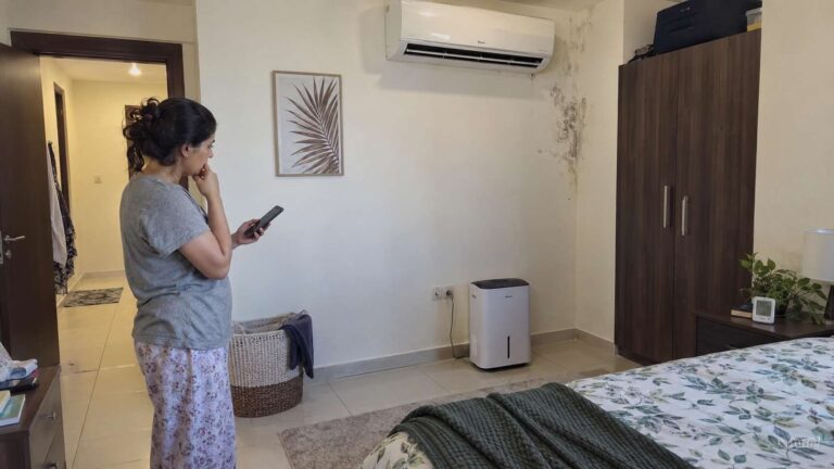 Resident checking a damp mold-prone area and indoor humidity in a UAE apartment