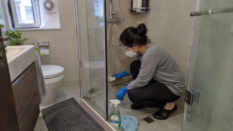 Homeowner wearing gloves, sealed goggles, N95 respirator, and non-slip footwear while cleaning small shower mold