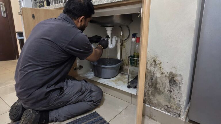 Plumber repairing an active leak near visible mold damage in a UAE apartment