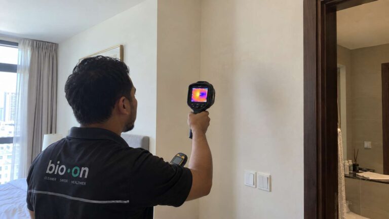 Inspector scanning a residential wall with a thermal camera while checking for hidden moisture.