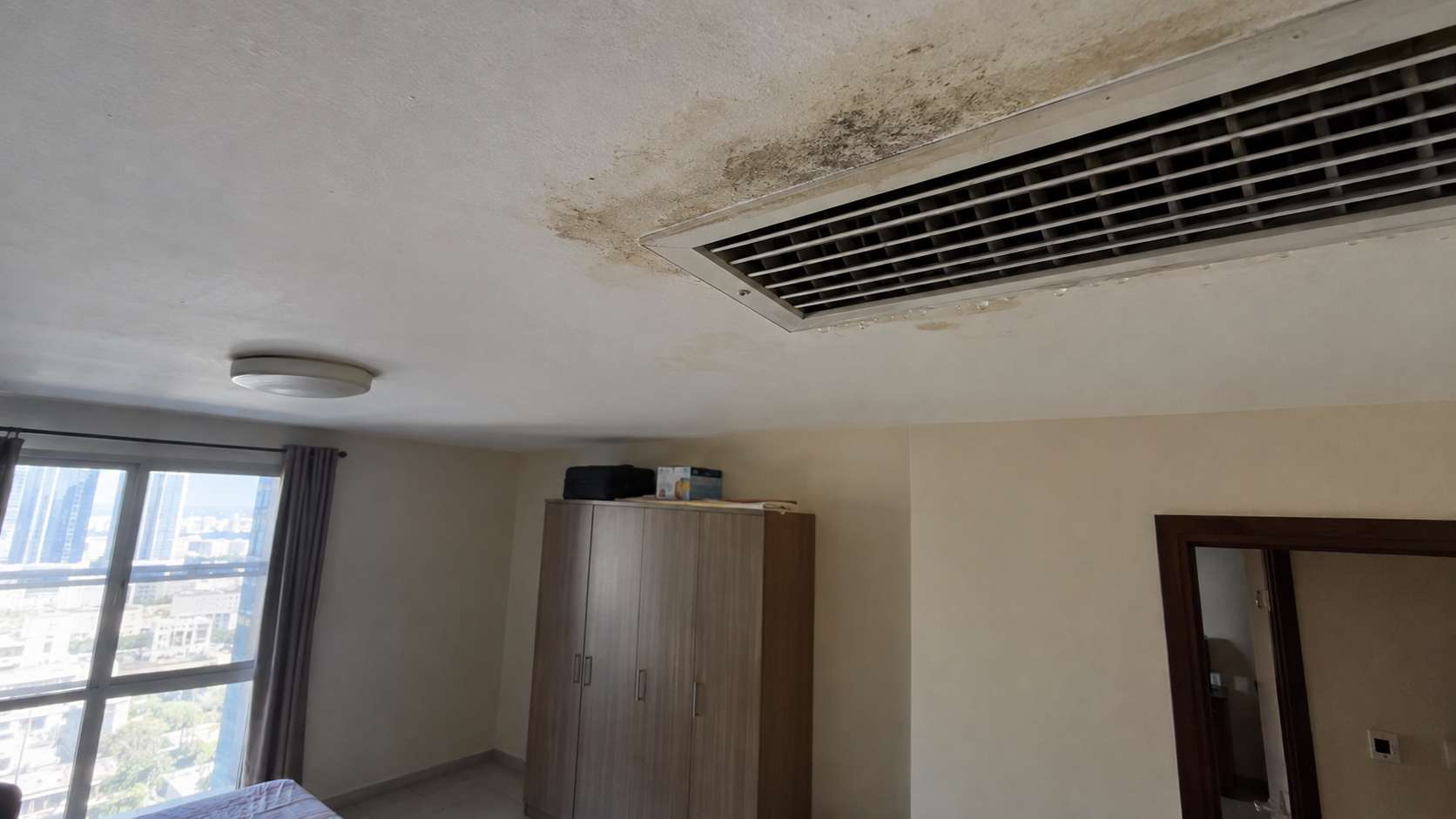 Condensation and localized mold spotting around a ceiling AC grille in a UAE bedroom.
