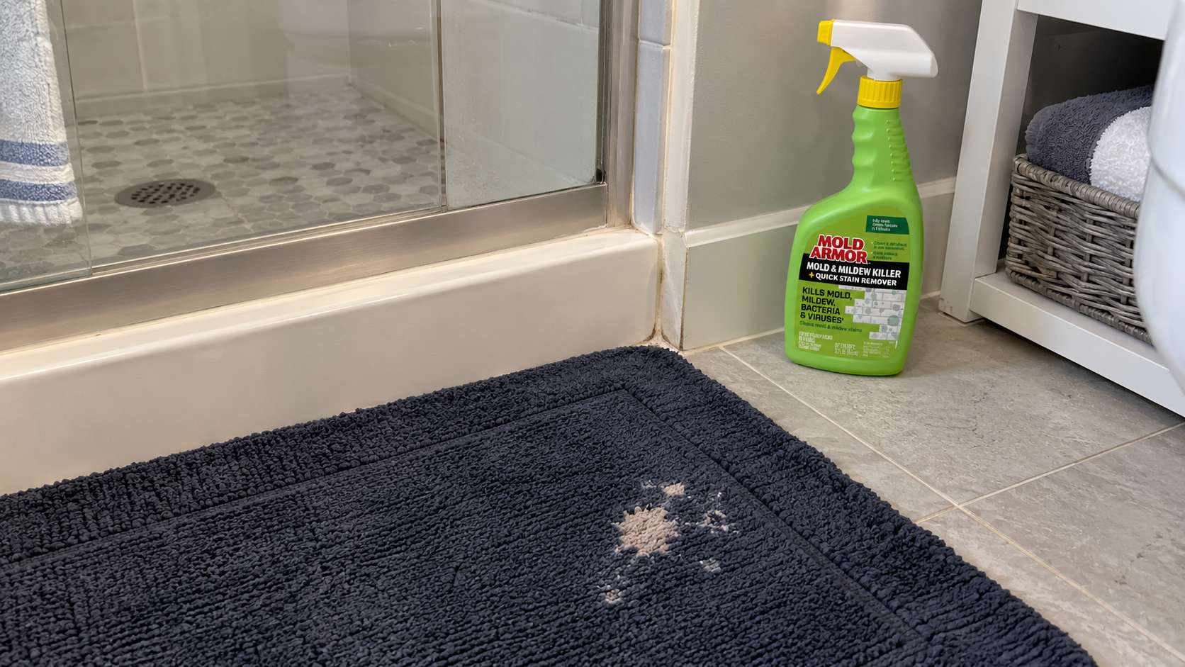 Bleach-discolored bath mat beside a Mold Armor stain remover bottle in a bathroom.