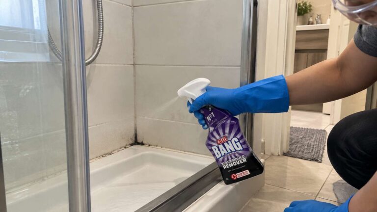 Homeowner applying Cillit Bang Black Mould Remover to a small black mould stain in a ventilated bathroom.