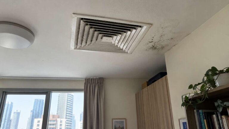 Ceiling AC vent with dry gray dust buildup and localized moisture-related spotting nearby.