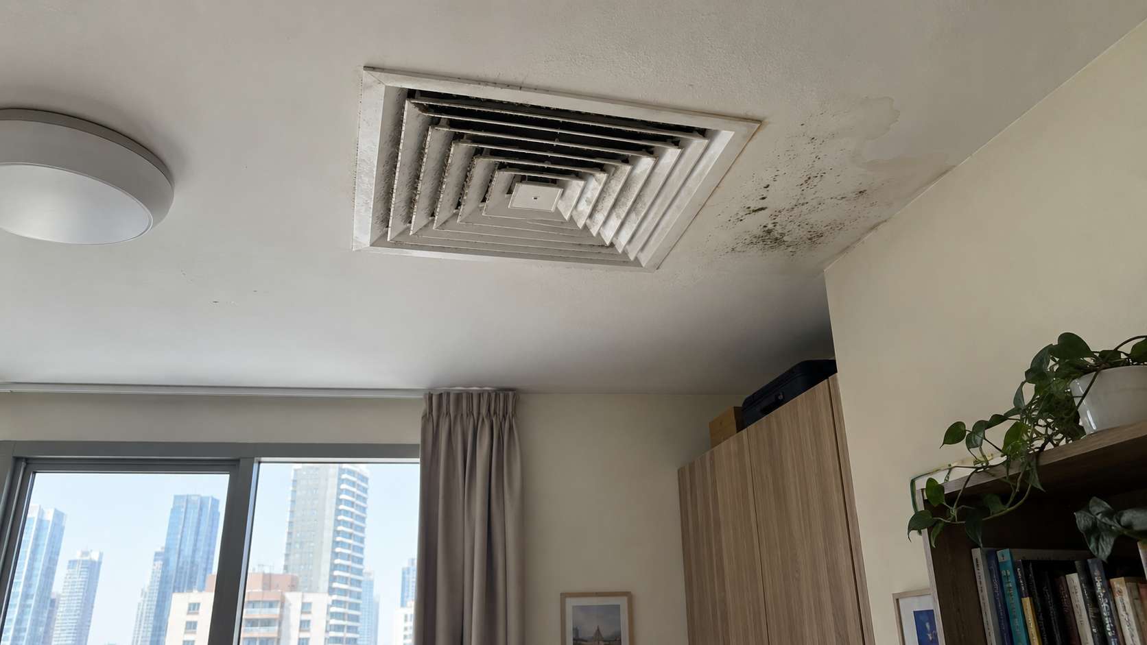Ceiling AC vent with dry gray dust buildup and localized moisture-related spotting nearby.