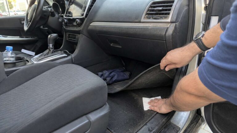 Car owner checking damp carpet under the passenger floor mat as a possible source of musty odor.