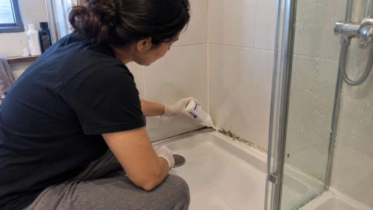 Homeowner applying mold remover gel to stained silicone in a tiled shower.