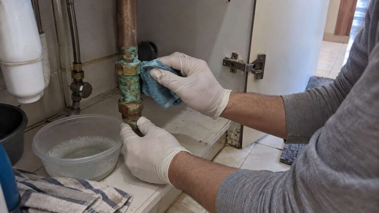 Homeowner gently cleaning green corrosion from a copper pipe with a soft cloth.