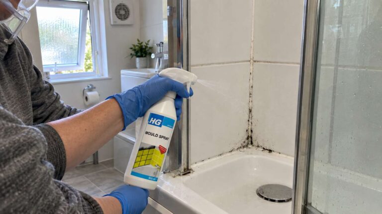 Homeowner applying HG Mould Spray to stubborn black mould stains around bathroom grout and silicone.