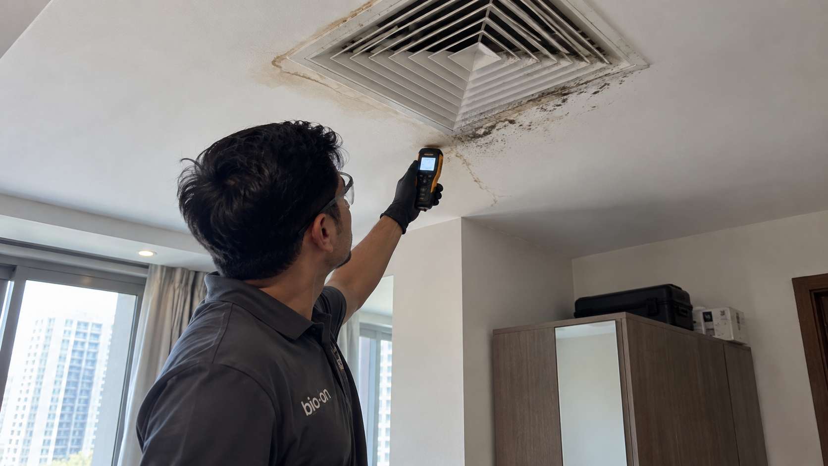 Bio-On technician checking moisture around a spotted ceiling AC vent with a handheld meter.