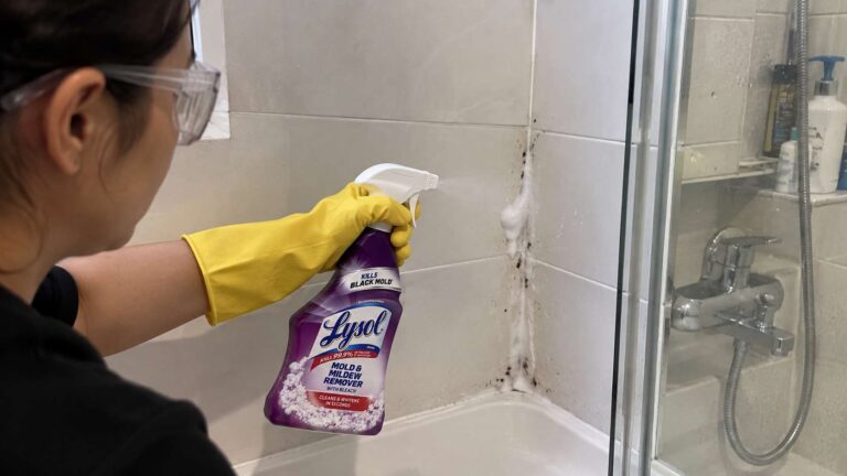 Homeowner applying Lysol mold and mildew cleaner to stained grout in a ventilated shower.