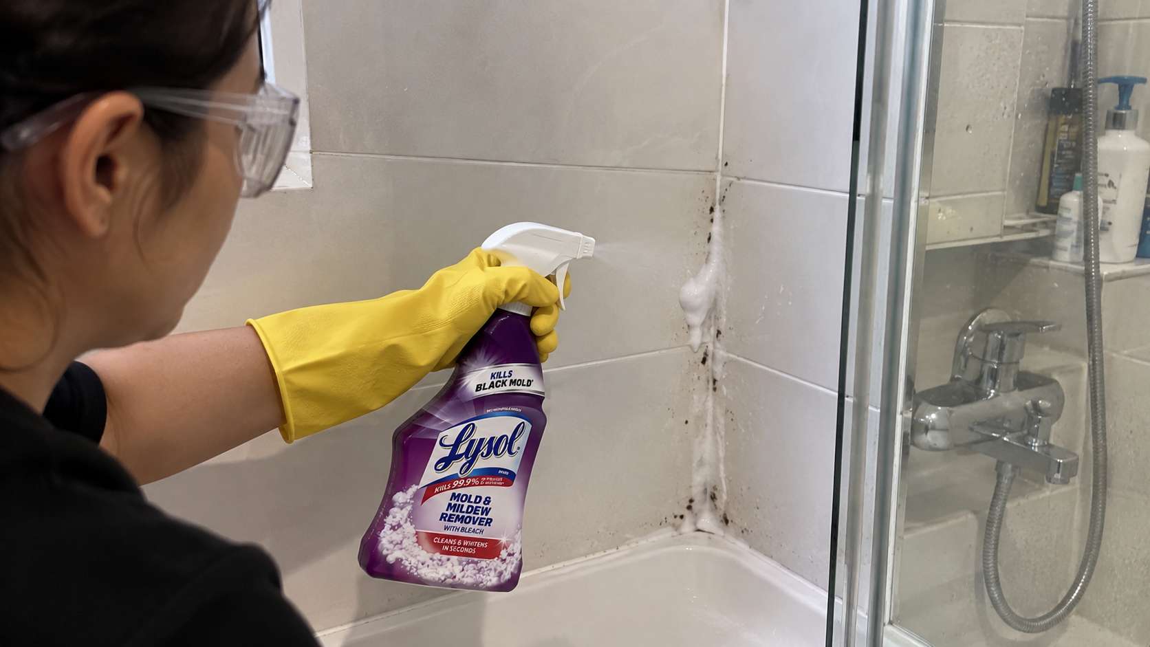 Homeowner applying Lysol mold and mildew cleaner to stained grout in a ventilated shower.