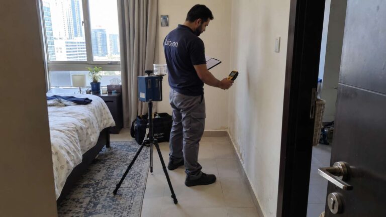 Mold inspector collecting an indoor air sample in a room with subtle signs of moisture damage.
