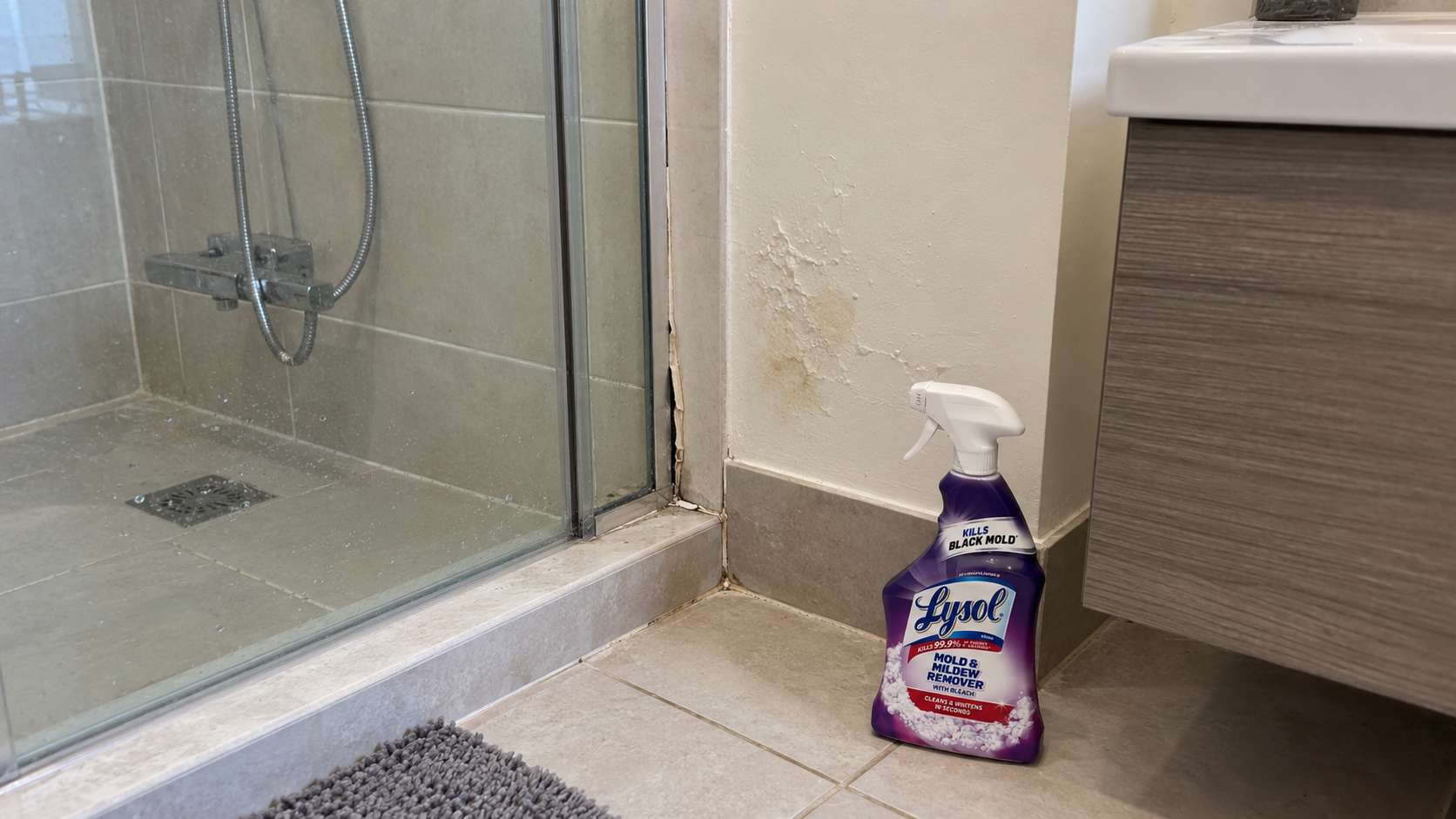 Lysol cleaner beside a shower joint with failed caulk and moisture-damaged wall finishes.